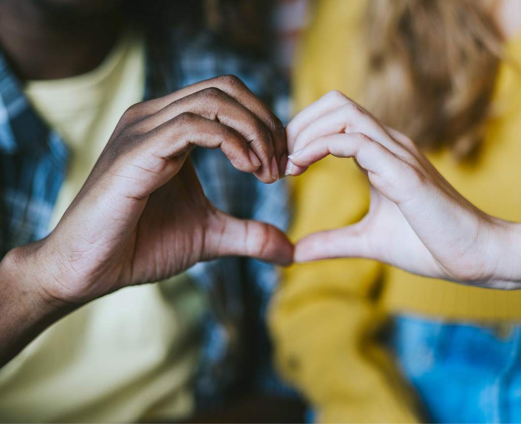 One hand from two different women creating a heart shape