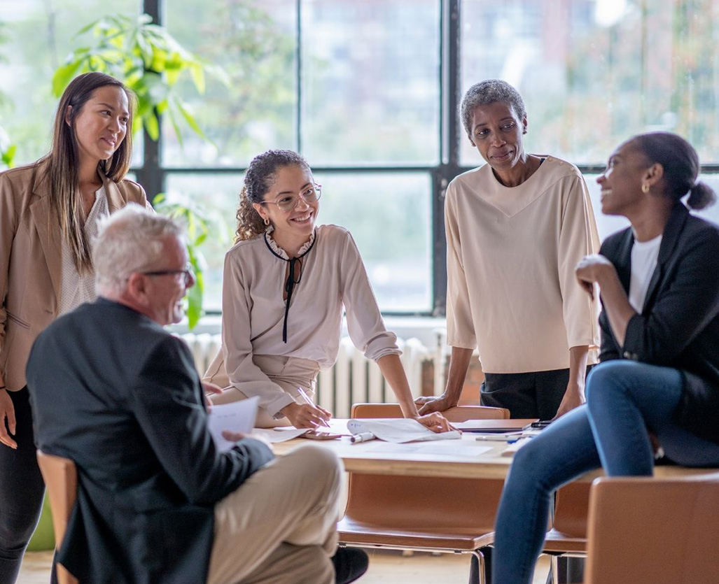 Workplace Campaigns - four women and one man gathered around a table and discussing a topic