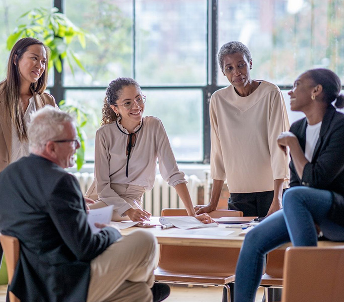 Workplace Campaigns - four women and one man gathered around a table and discussing a topic